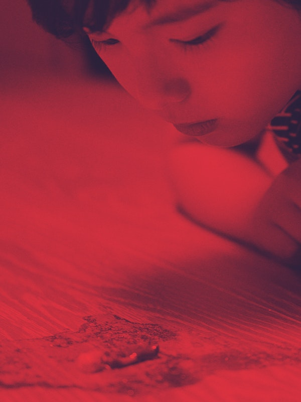 Boy bathes in read light, looking at a tiny figurine of the Little Prince.